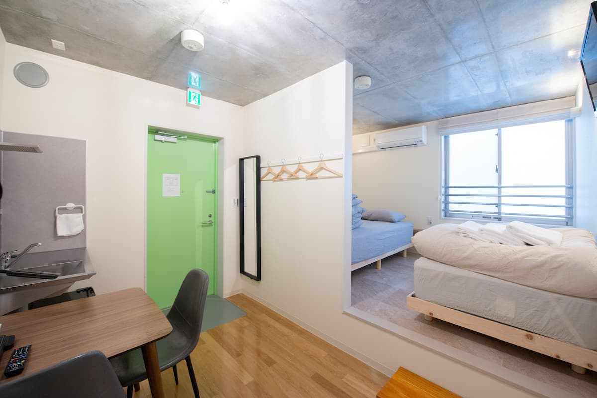 Una habitación con puerta verde, una cama, un escritorio y una silla.