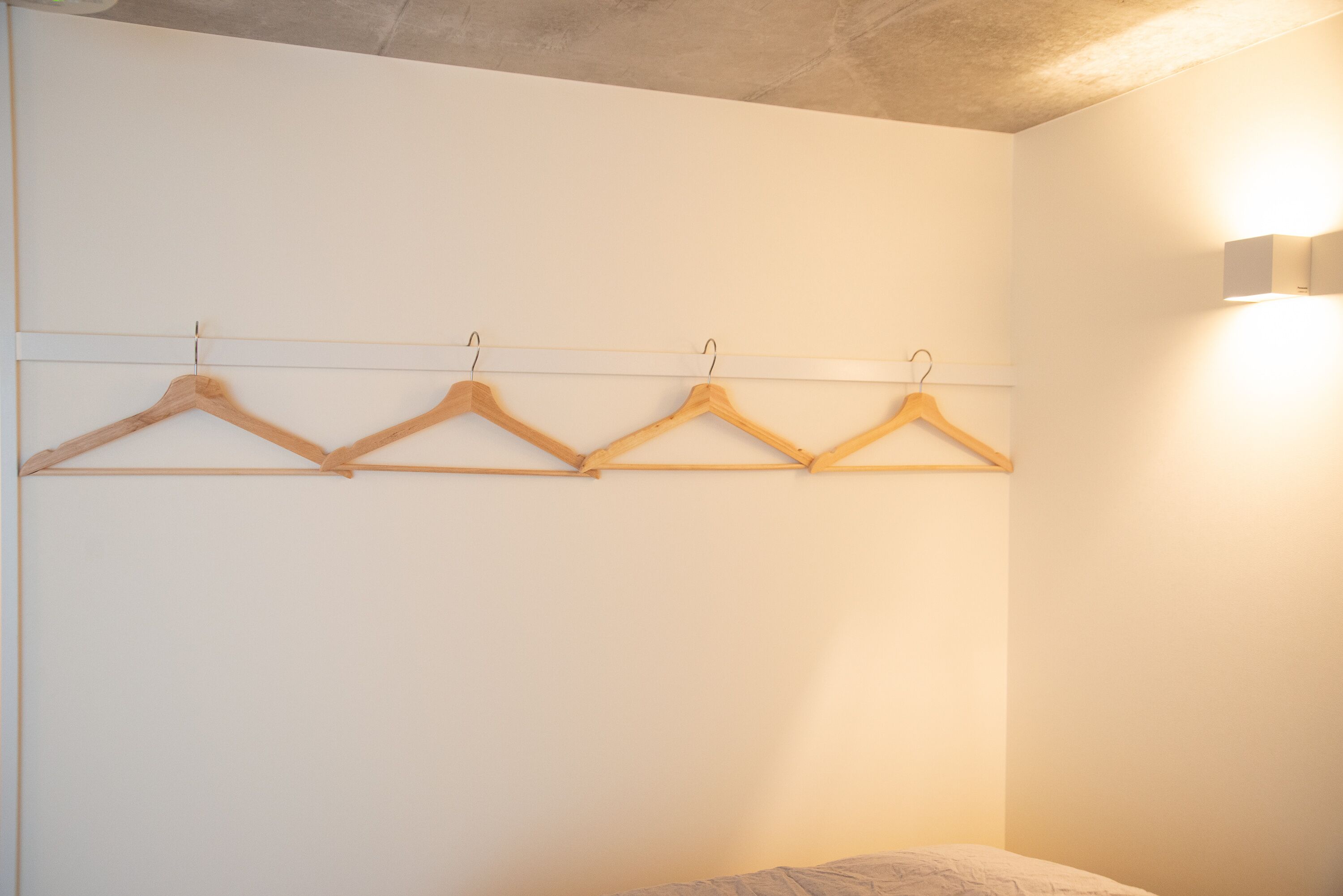 Un dormitorio con una cama, un perchero de madera y una lámpara fijada a la pared.