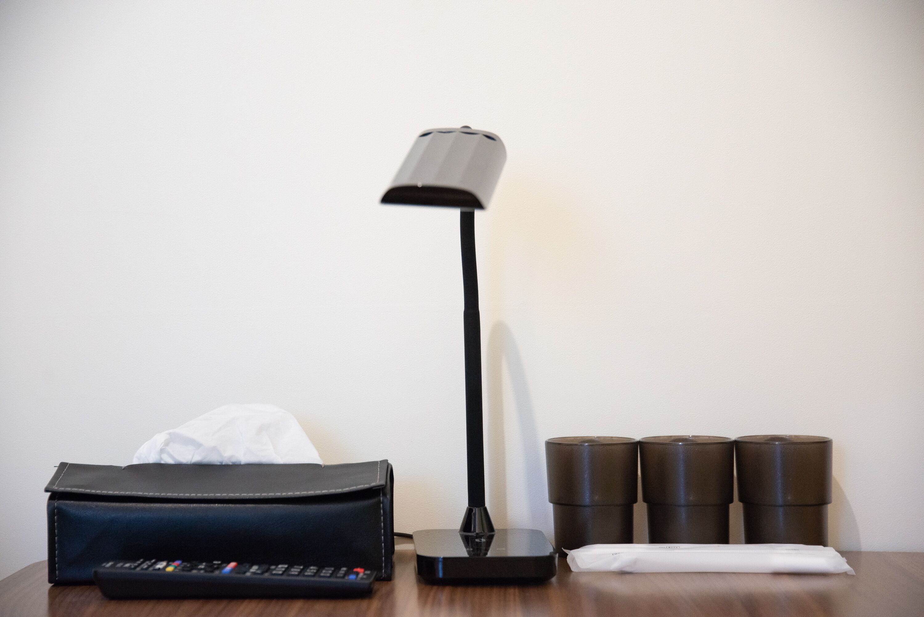 A remote control, a black lamp, a black leather bag, and a white tissue on a wooden surface.