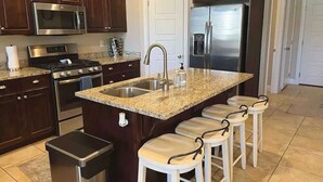 A kitchen with dark wood cabinets, stainless steel appliances, a granite countertop, and a bar stool area. - Poolside Adventures: FREE State and National Parks Passes! (Washington)
