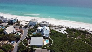 Vue aérienne d’une propriété située sur la côte, comprenant plusieurs bâtiments, une plage et une piscine.