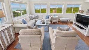 A modern living room with a sofa, armchairs, a coffee table, a TV, and large windows with a view of the ocean. - 30A Beachfront and State Park Views, Gulf Trace (Santa Rosa Beach)
