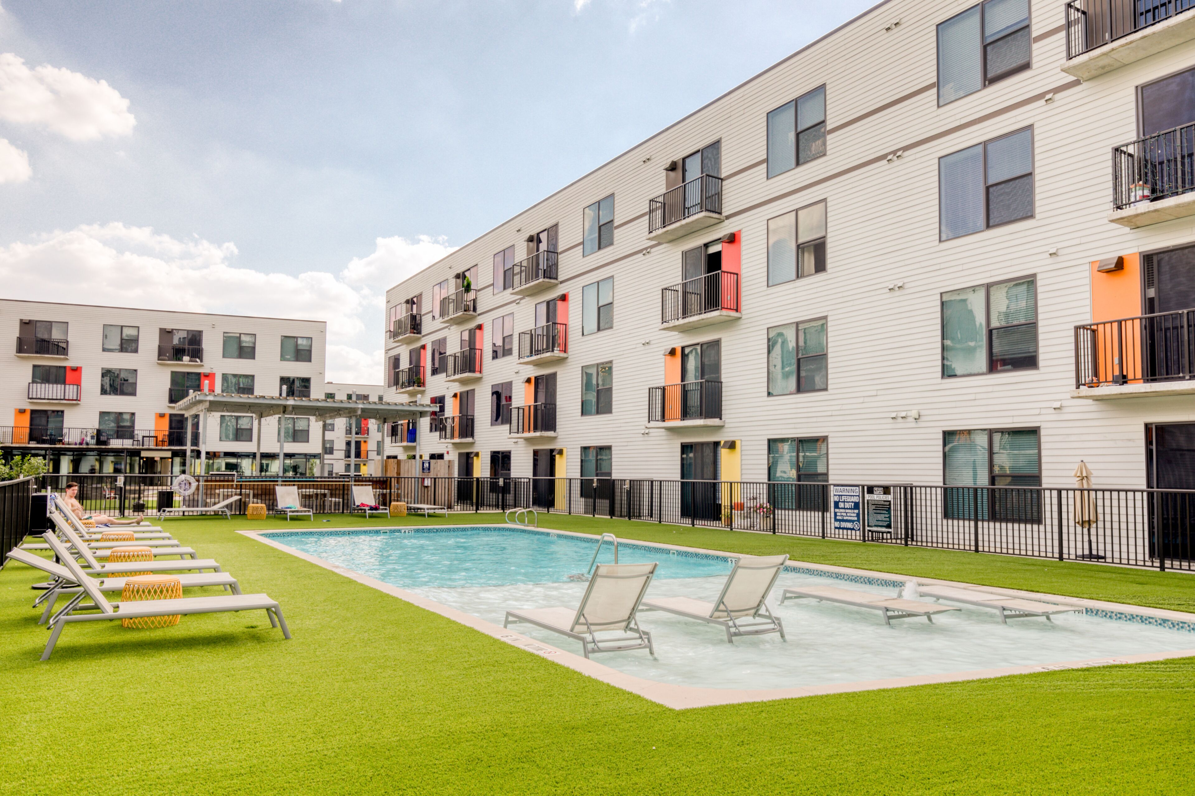 A modern apartment building with a swimming pool, outdoor seating, and balconies.