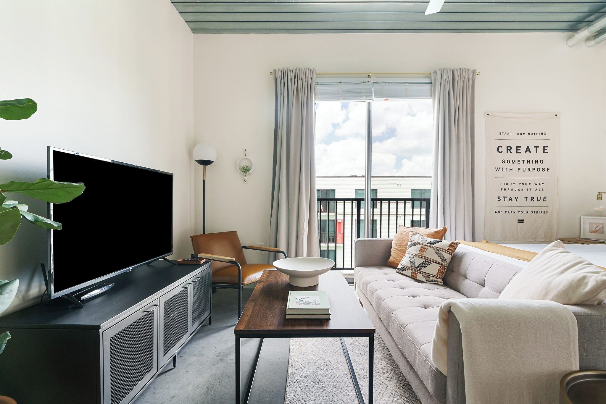 A modern living room with a flat-screen TV, a wooden coffee table, a sofa, and a large window with curtains.