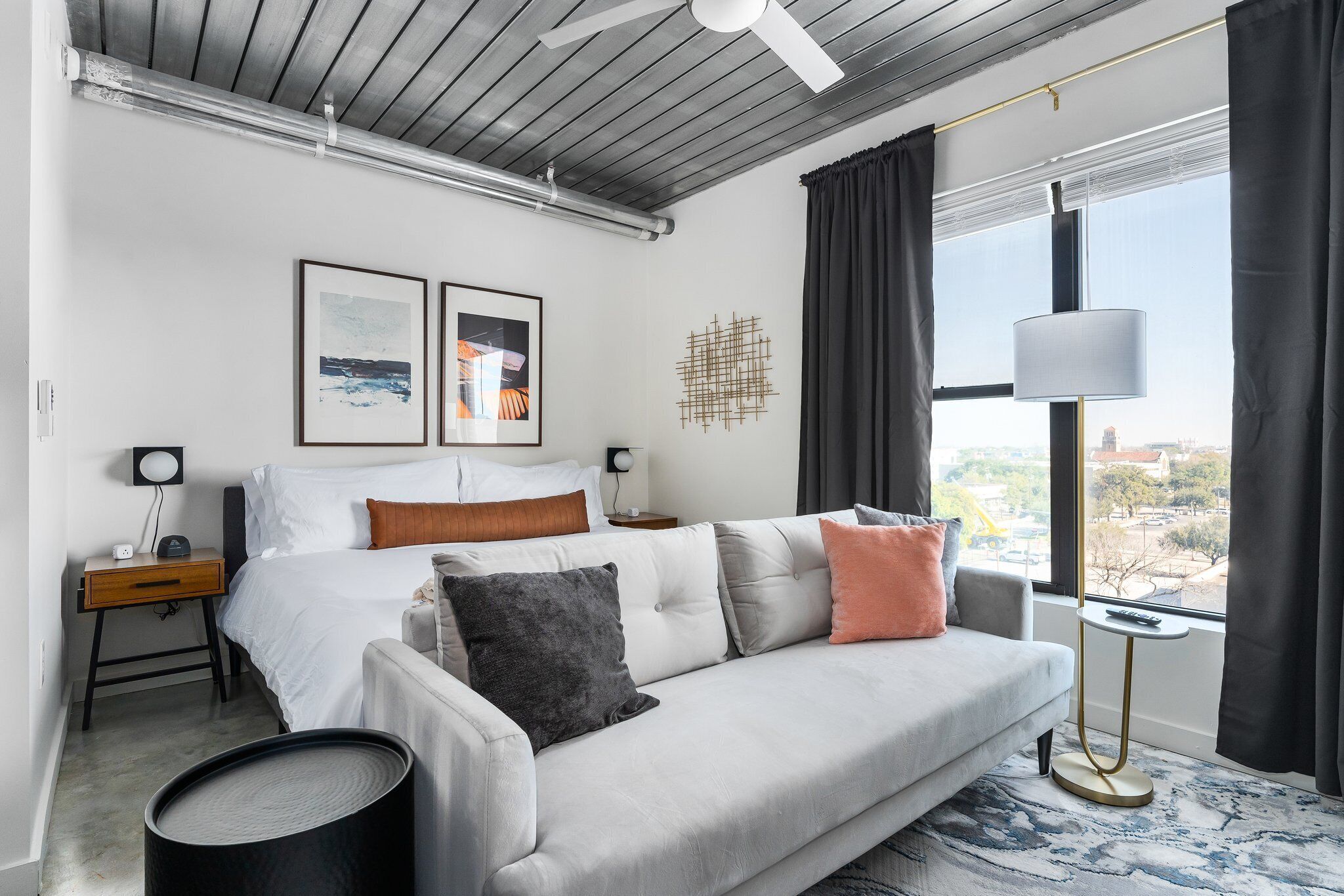 A modern hotel room with a bed, a sofa, a desk, and a window with curtains.