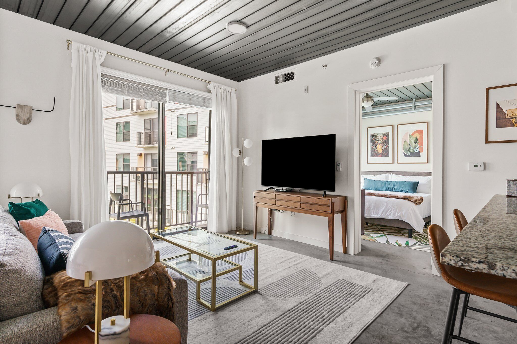 A modern living room with a flat-screen TV, a glass coffee table, a sofa, and a dining area with a table and chairs.