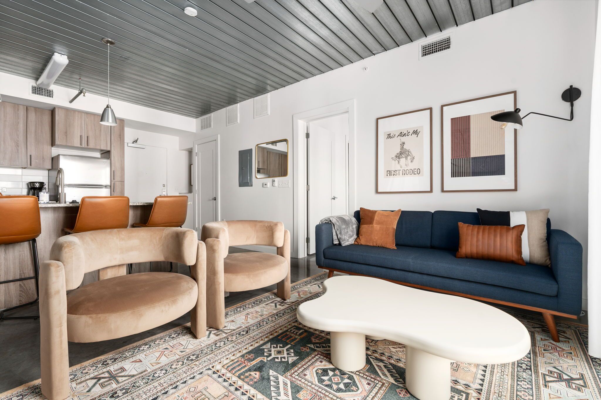 A modern living room with a sofa, chairs, a coffee table, and a kitchen in the background.
