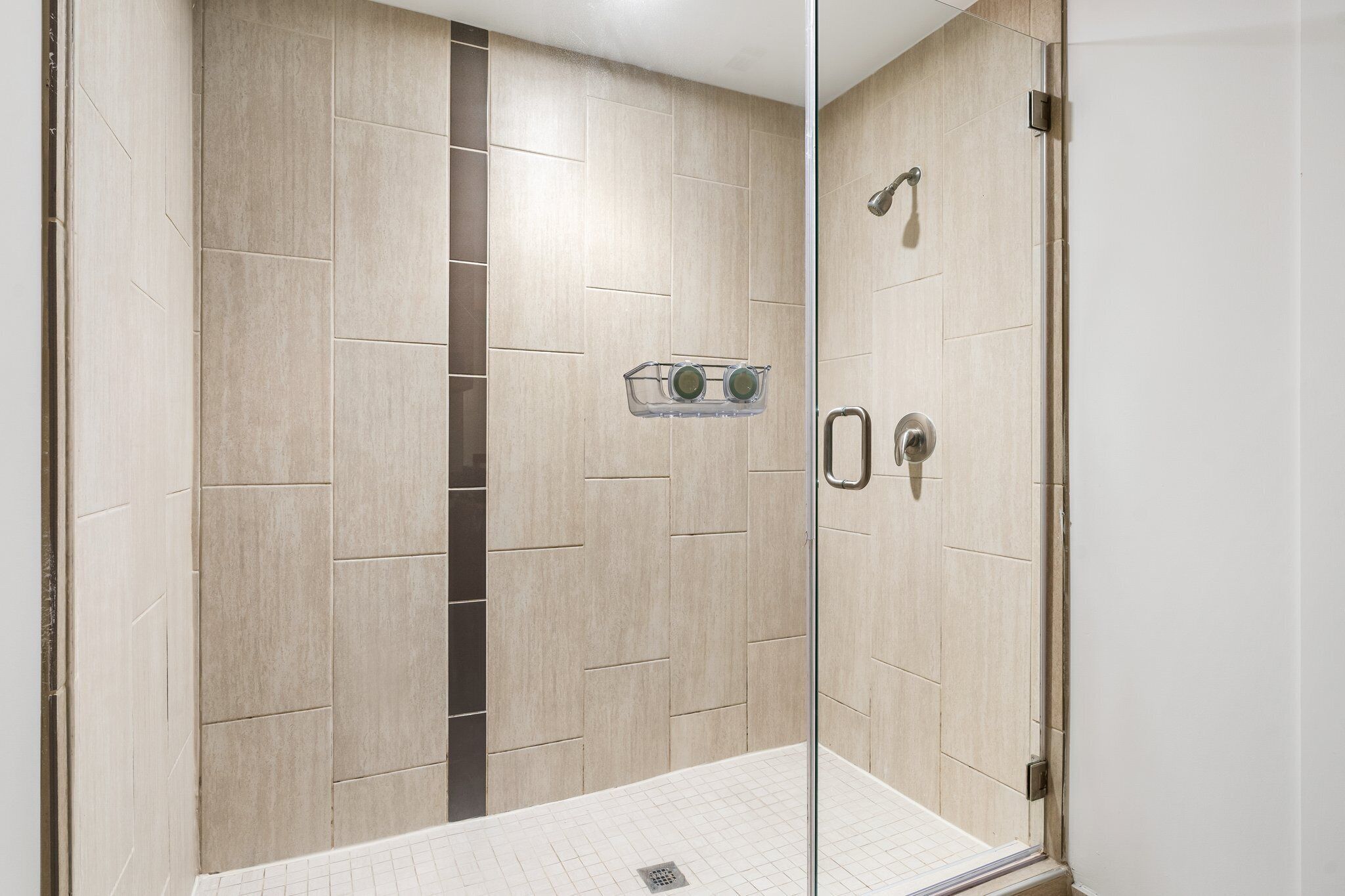 Une douche moderne avec des carreaux de couleur beige, une porte en verre et une poignée en métal.