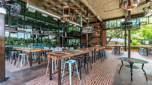 Een ruim café met hoge plafonds, zichtbare ventilatiekanalen en grote ramen met uitzicht op het omliggende landschap.