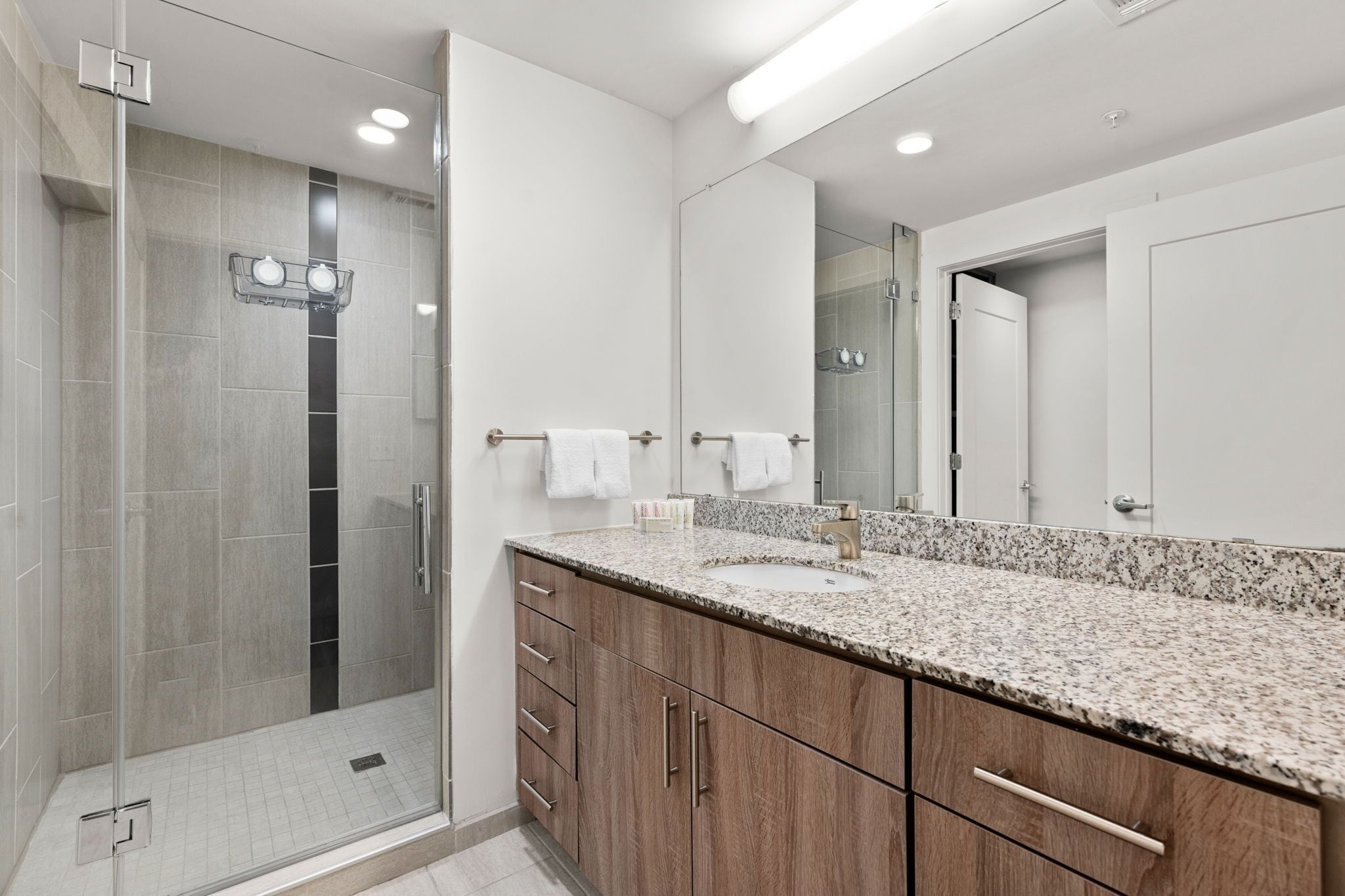 Une salle de bain moderne avec une douche à parois de verre, un grand miroir et un comptoir en granit.