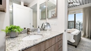 Een moderne badkamer met een granieten aanrecht, een grote spiegel en een potplant.