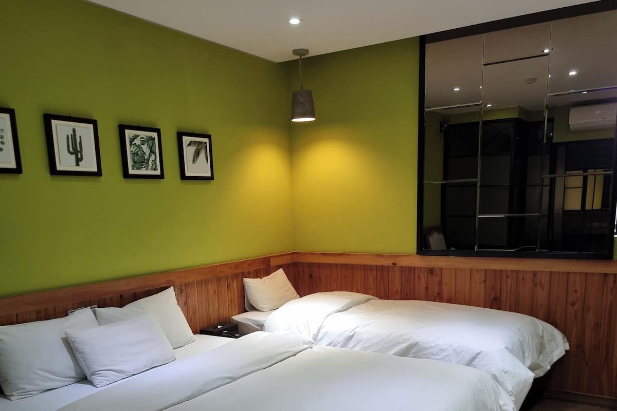 Habitación de hotel con dos camas, cabecera de madera, pared verde y obras de arte enmarcadas.