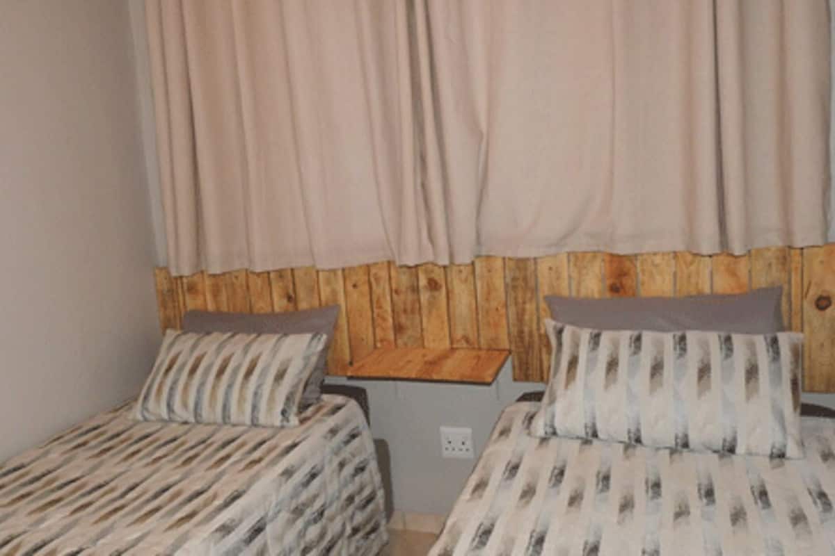 A small, cozy room with two single beds, wooden headboard, and a neutral color scheme.
