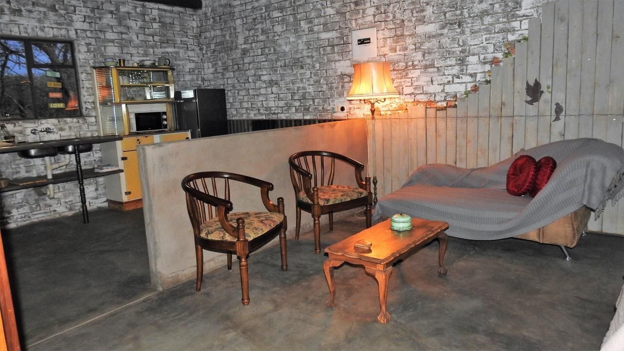 Een gezellige zithoek met een bank, twee houten stoelen, een salontafel en een metselwerk muur.
