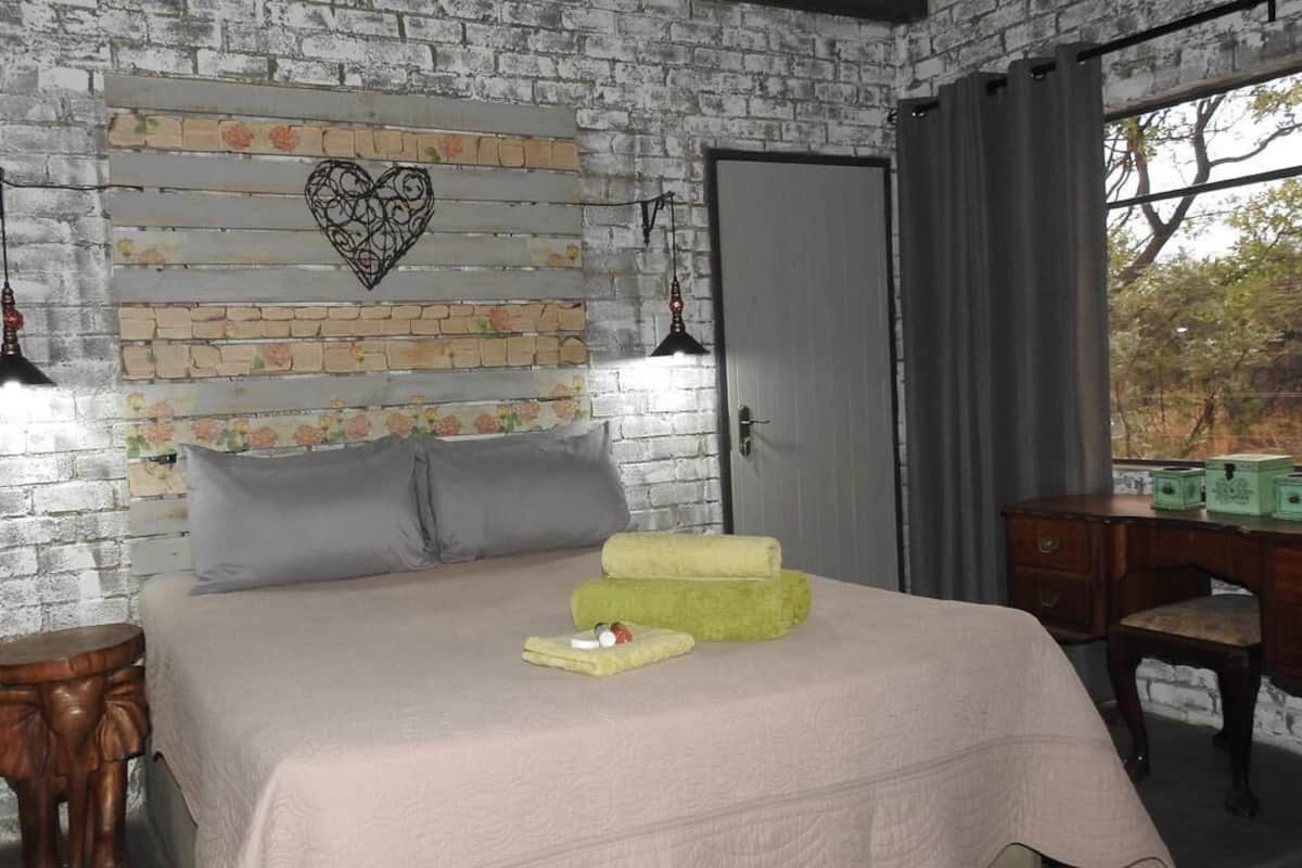 A bedroom with a brick-patterned headboard, a bed with pillows, a bedside table, and a desk with drawers.