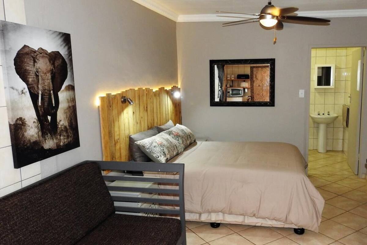 A bedroom with a bed, a wooden headboard, a ceiling fan, a bathroom with a sink, and a mirror.