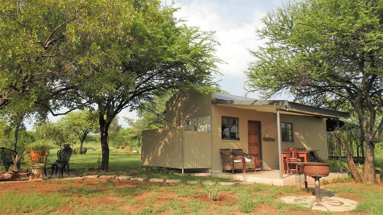 A small, single-story house with a flat roof, a porch with two chairs, and a small table.