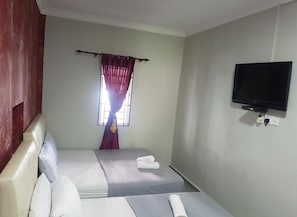 A small, simple room with two beds, a TV on the wall, and a window with curtains.
