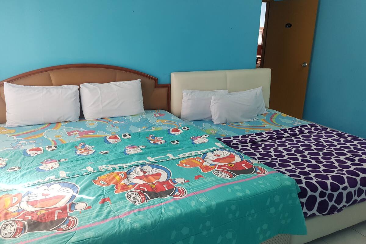 Un llit amb un llençol de colors que representa personatges de dibuixos animats, un capçal i almoadines blanques.