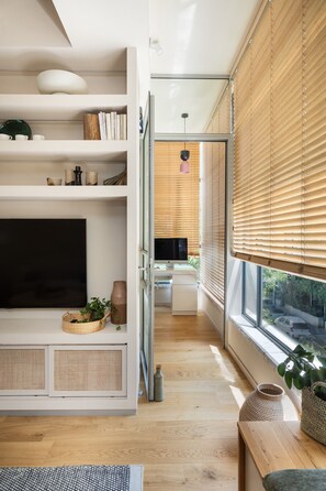 A modern living room with a TV, shelves, and a window with blinds. - Old North Hidden Treasure 2BR 2BA (Tel Aviv)