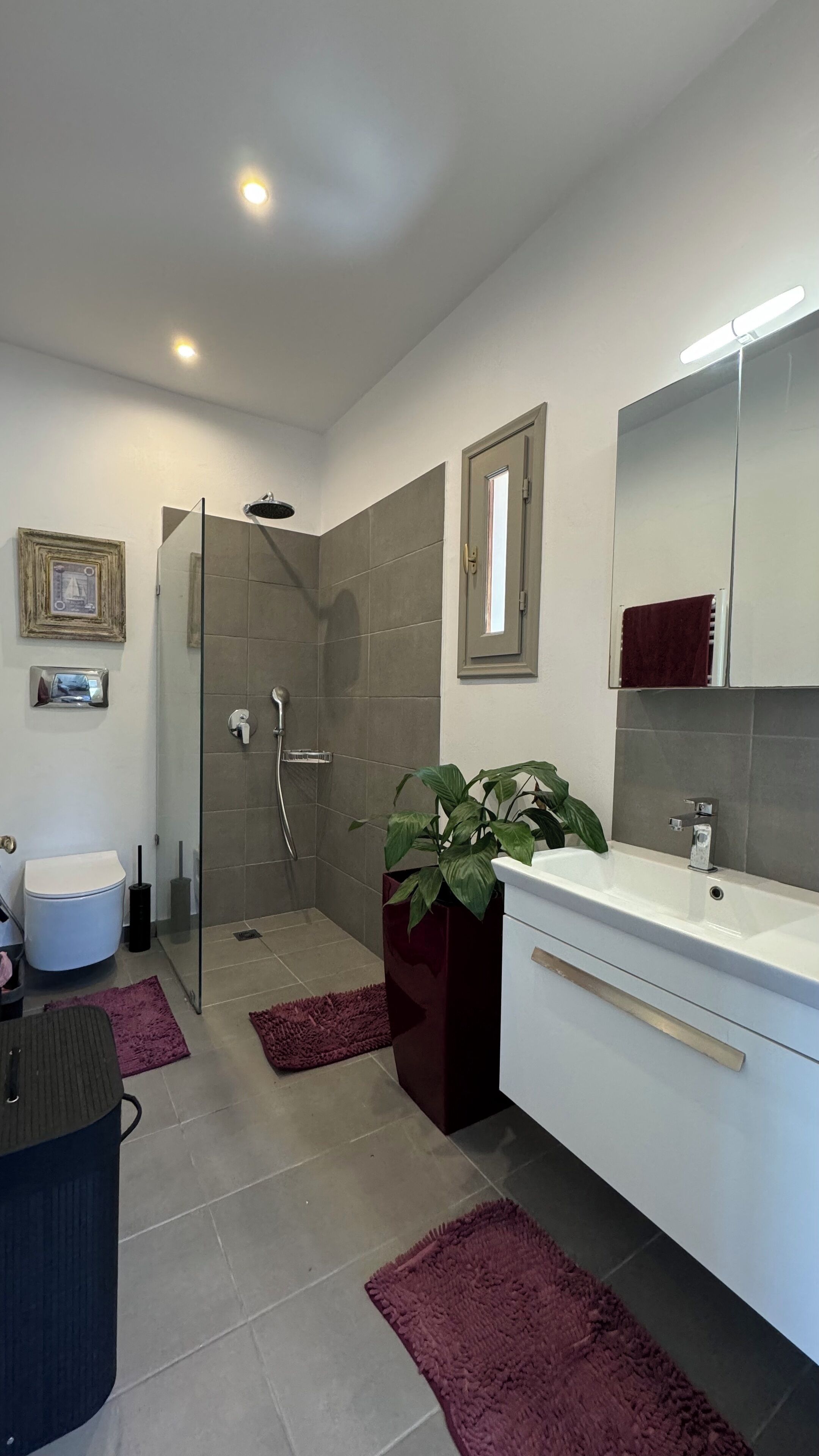 A modern bathroom with a walk-in shower, a large mirror, and a white vanity.