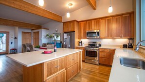 A modern kitchen with wooden cabinets, a stainless steel refrigerator, a microwave, and an island with a sink. - Blackberry Bramble - Beckoning Views, Peaceful Elegance, Walk to Downtown (Hood River)