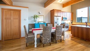 A modern kitchen with wooden cabinets, a central island, and a dining area with patterned chairs. - Blackberry Bramble - Beckoning Views, Peaceful Elegance, Walk to Downtown (Hood River)
