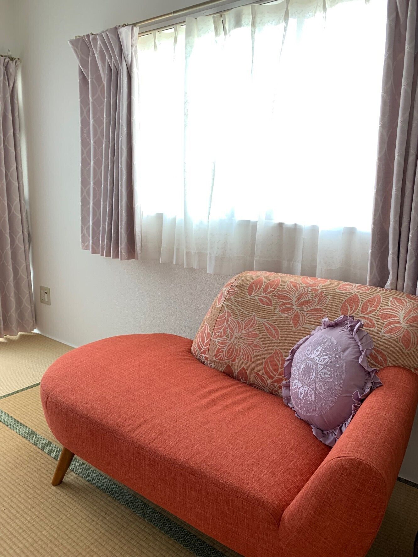 A room with a red sofa, a patterned pillow, and a window with sheer curtains.