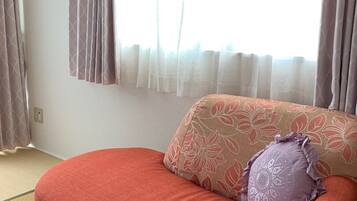 A room with a red sofa, a patterned pillow, and a window with sheer curtains.