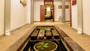 A spacious hallway with a central water feature, wooden benches, and a traditional door leading to a room. - Ali Gedara Bungalow (Galle)
