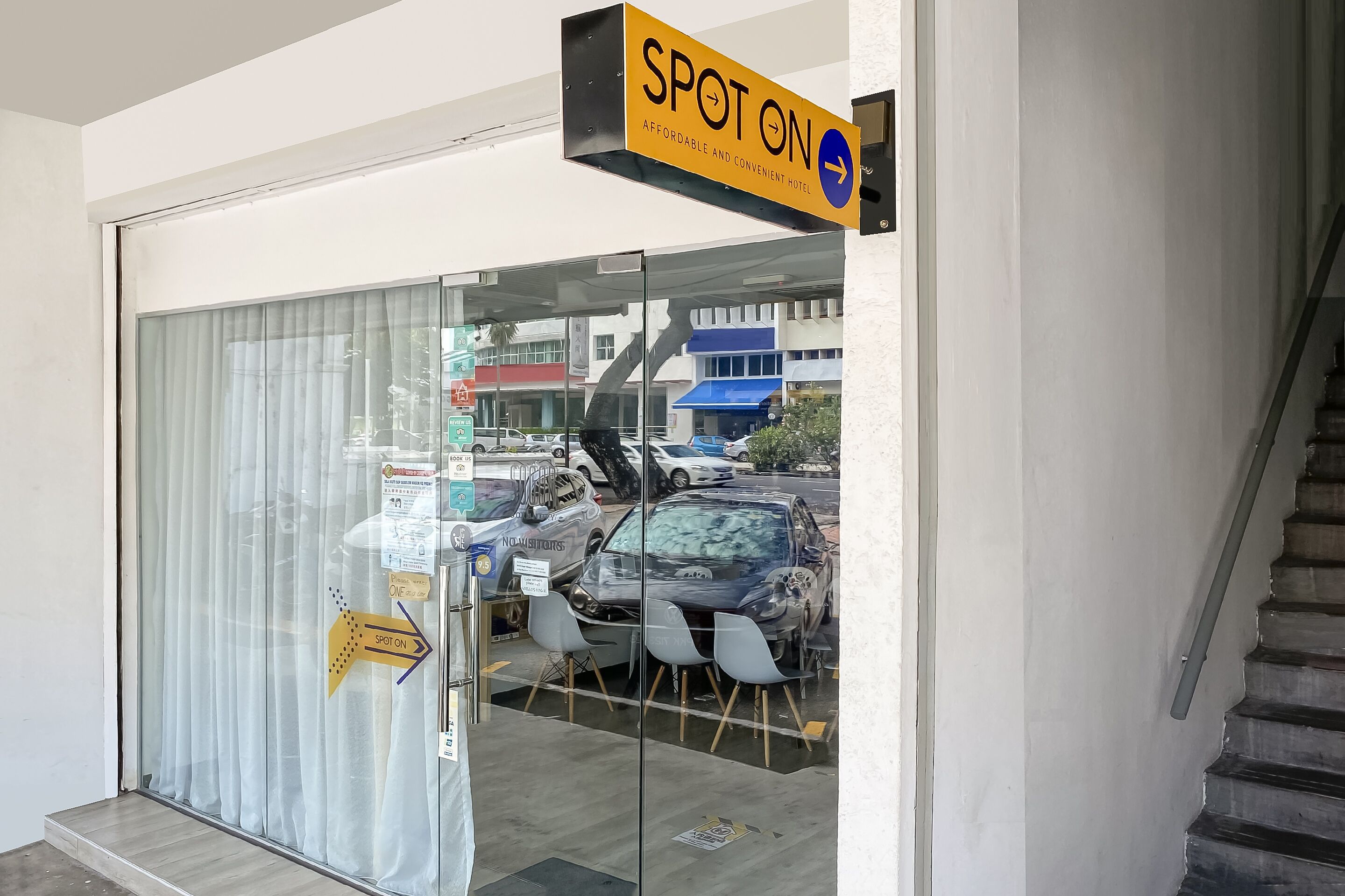 A hotel entrance with a glass door, a sign reading "SPOT ON AFFORDABLE AND CONVENIENT HOTEL," and a staircase to the right.