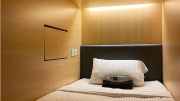 A small, cozy hotel room with a single bed, a headboard, a bedside table, and a wall-mounted light fixture.