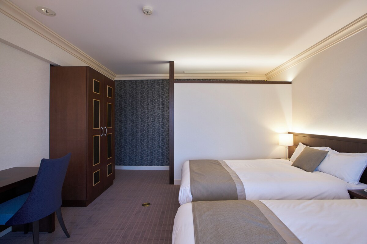 Een hotelkamer met twee bedden, een bureau en een stoel.