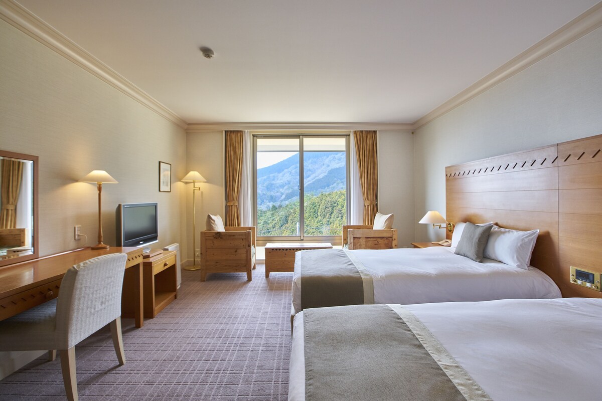 Een hotelkamer met twee bedden, een bureau, een televisie en een groot raam met uitzicht op de bergen.
