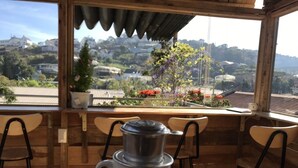 A rustic wooden table with a white coffee pot on a saucer, overlooking a scenic view of houses and greenery. - Tomorrow Homestay Da Lat (Xuan Huong - Da Lat)