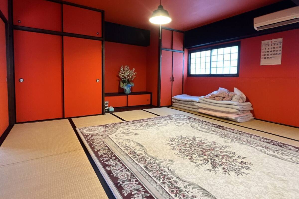 Een kamer met tatami matten, een groot tatami, een lage tafel met vaas en een raam met agenda.