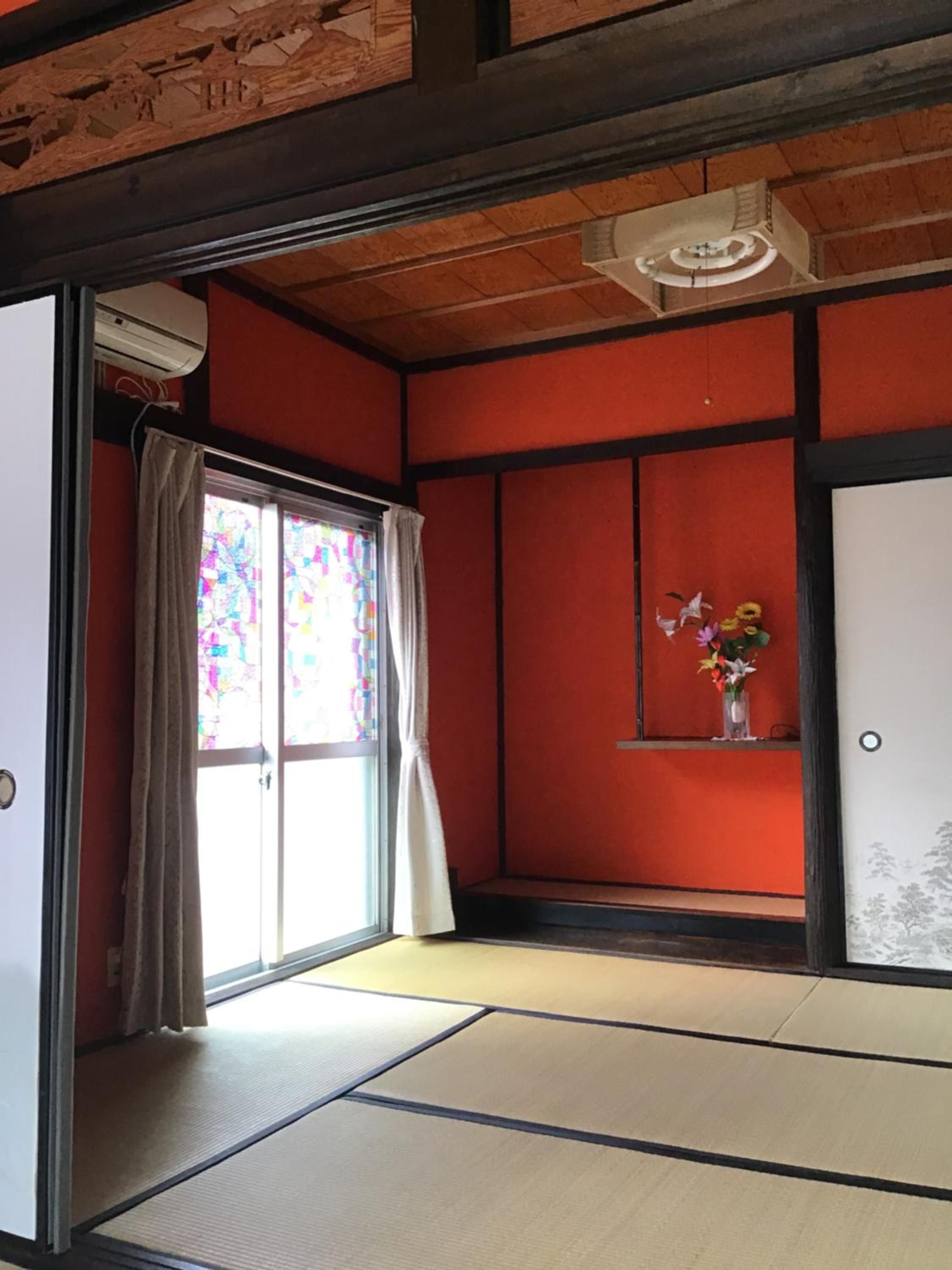 A traditional Japanese room with tatami flooring, a sliding door with a colorful stained glass window, and a small shelf with a vase of flowers.