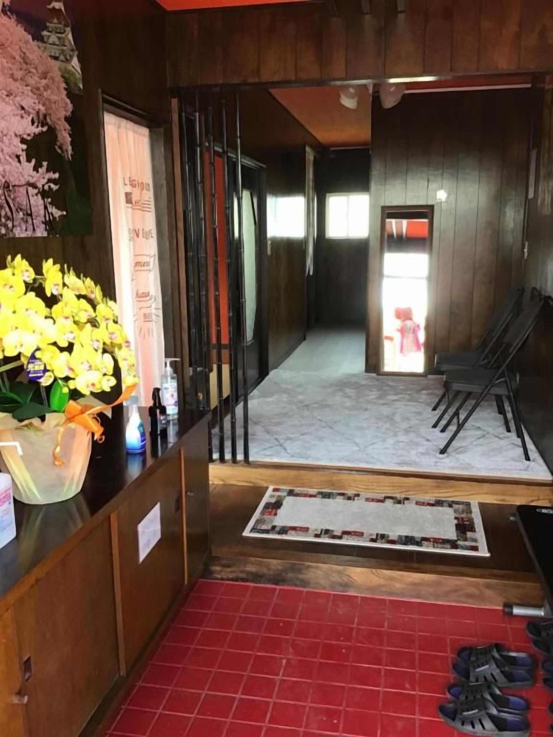 A reception area with a red carpet, a wooden counter with a plant, and a view into a hallway with a door and chairs.