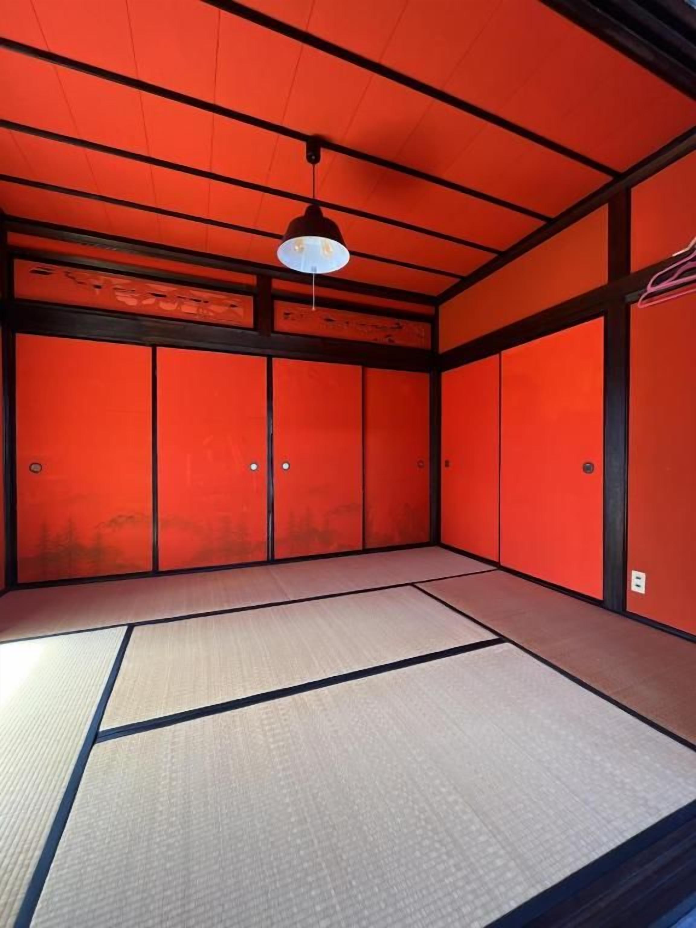 A room with tatami flooring, a hanging light fixture, and red walls.