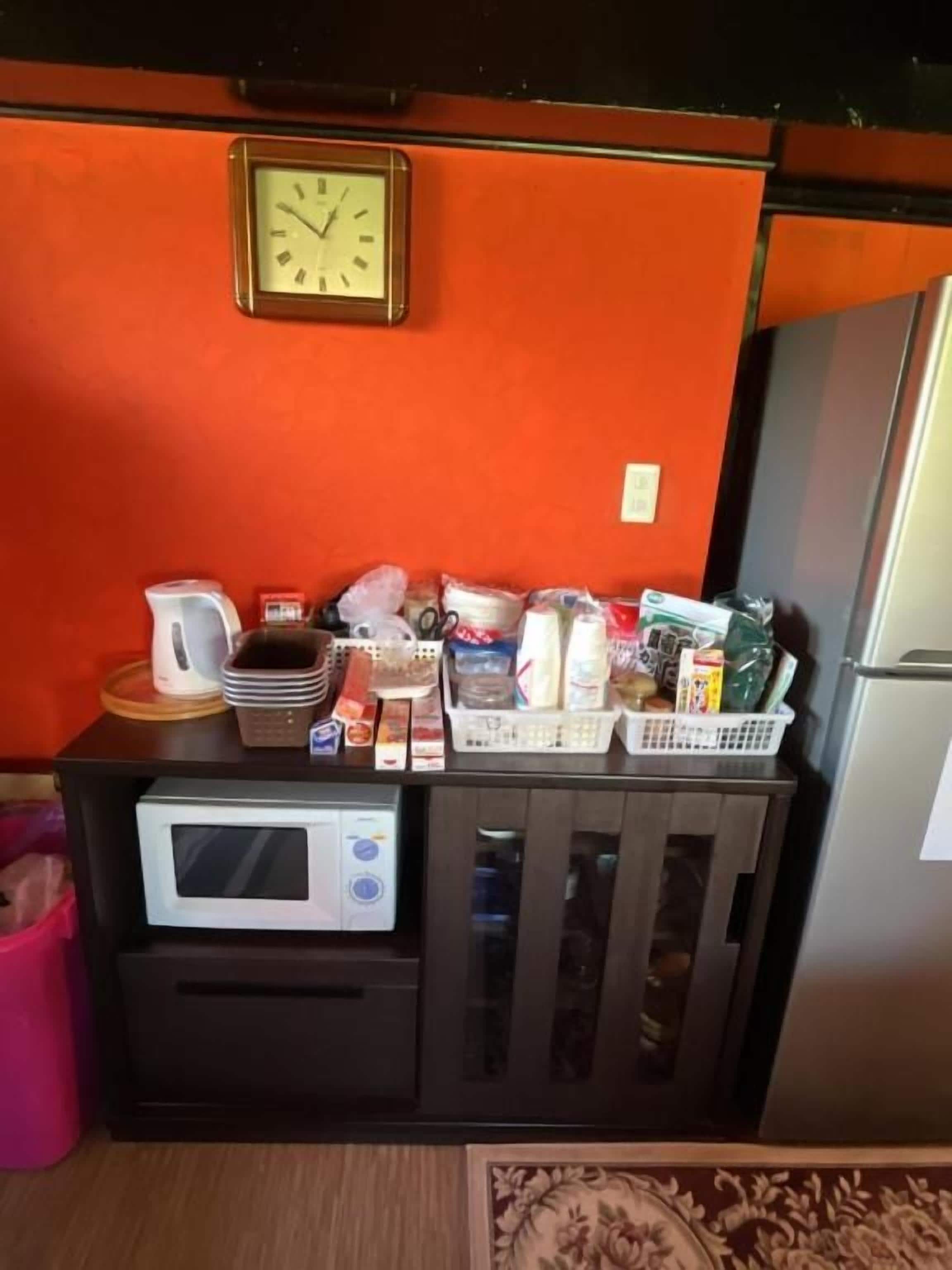 A kitchenette with a microwave, a clock, and various food items on the counter.