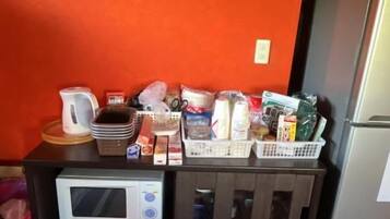 A kitchenette with a microwave, a clock, and various food items on the counter.