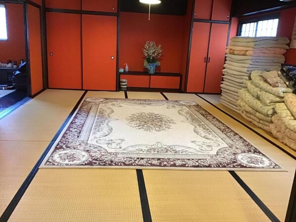 A tatami mat room with a central rug, a small table with a vase, and a stack of towels against the wall. - Airport Osaka (Kaizuka)