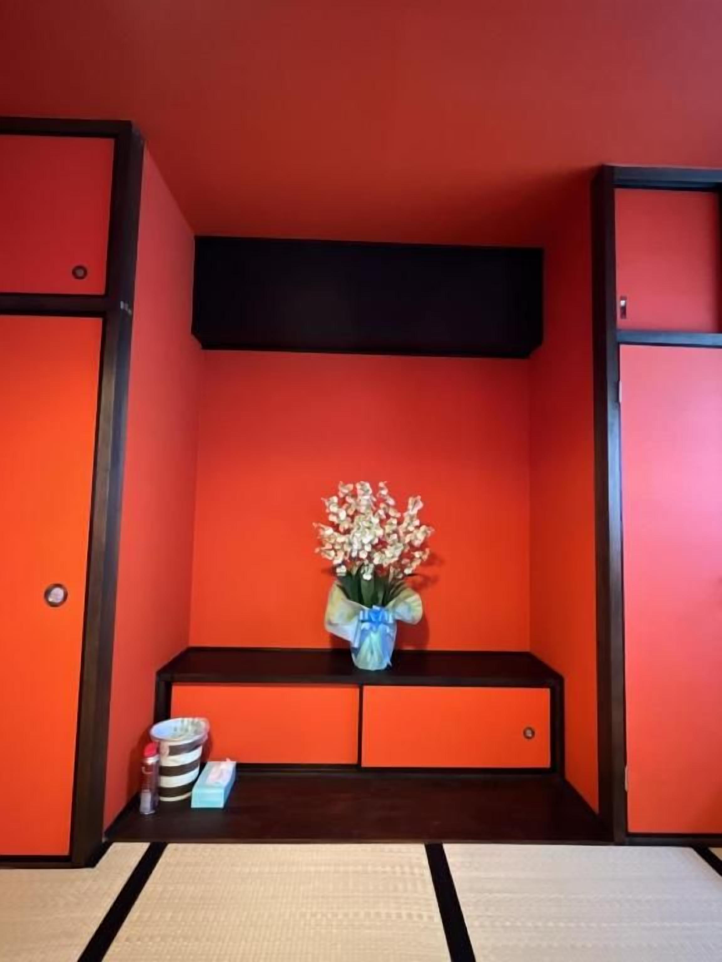 Um quarto com paredes vermelhas, um banco de madeira escura e um vaso com flores.