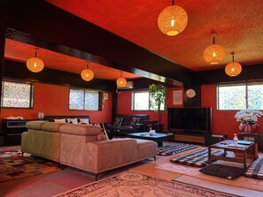A living room with a sofa, coffee table, and TV. There are windows with stained glass, a plant, and a clock on the wall. - Airport Osaka (Kaizuka)