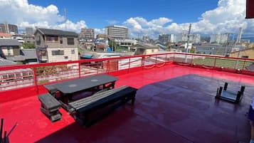 An outdoor terrace with a red floor, a picnic table, and a view of a cityscape.