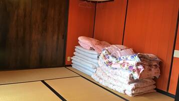 A room with tatami flooring, a wooden door, and a stack of bedding against the wall.