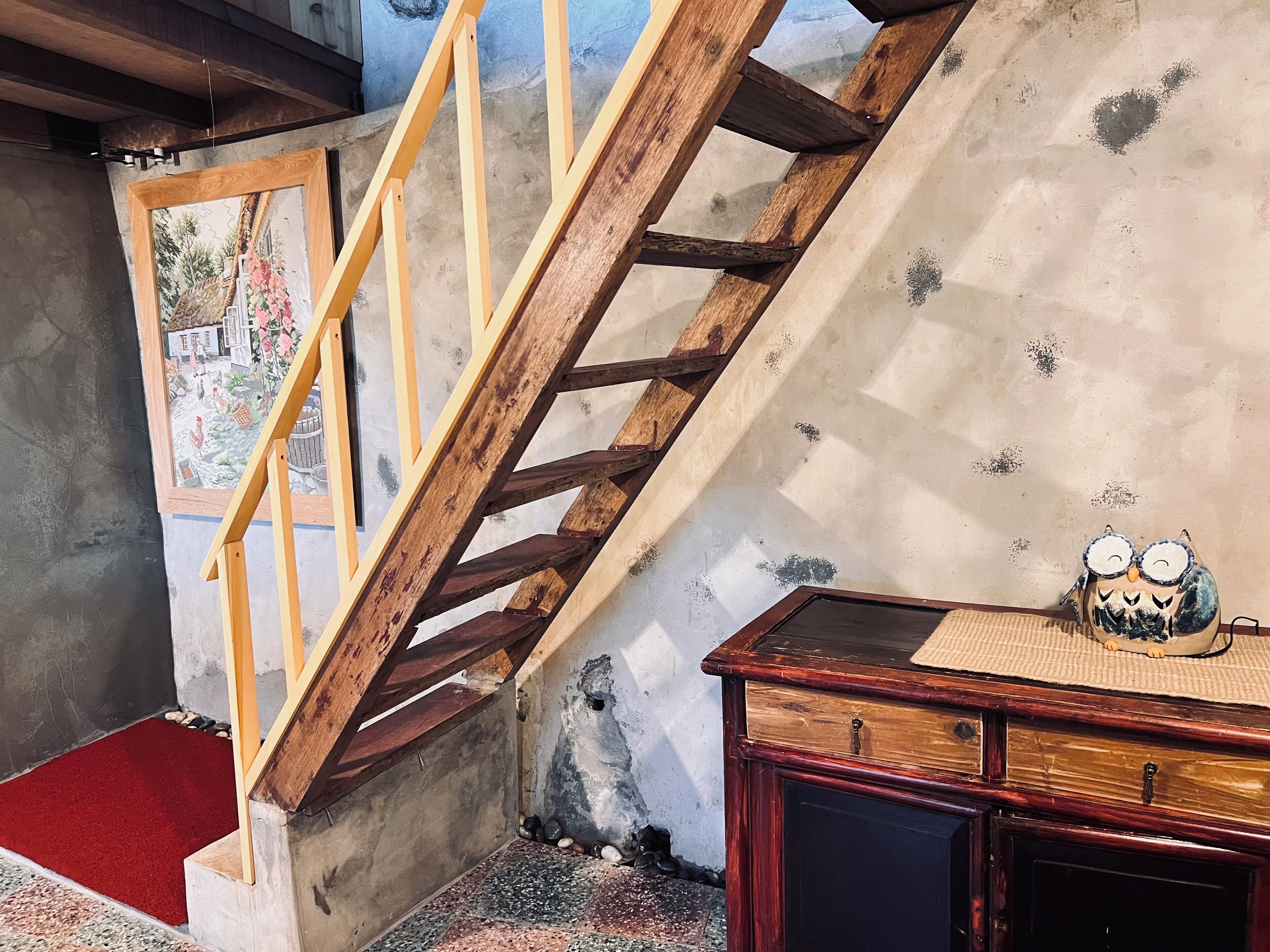 A wooden staircase leading to a room with a rustic wall and a wooden cabinet with a decorative owl.