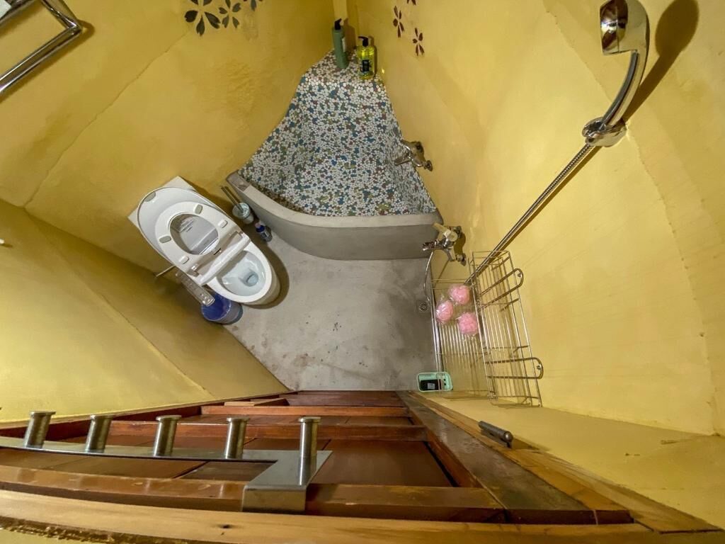 A bathroom with a toilet, a bathtub with a floral shower curtain, and a metal rack with pink balls.