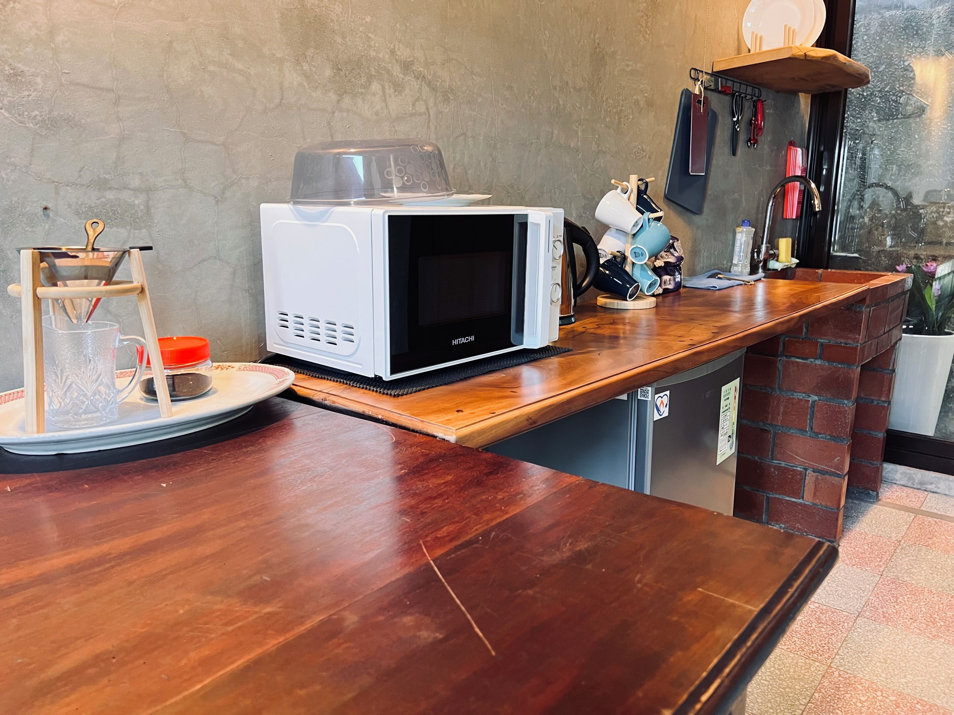 Een keuken met een witte magnetron op een houten aanrecht, een koffiezetapparaat en een klein rekje met keukengerei.