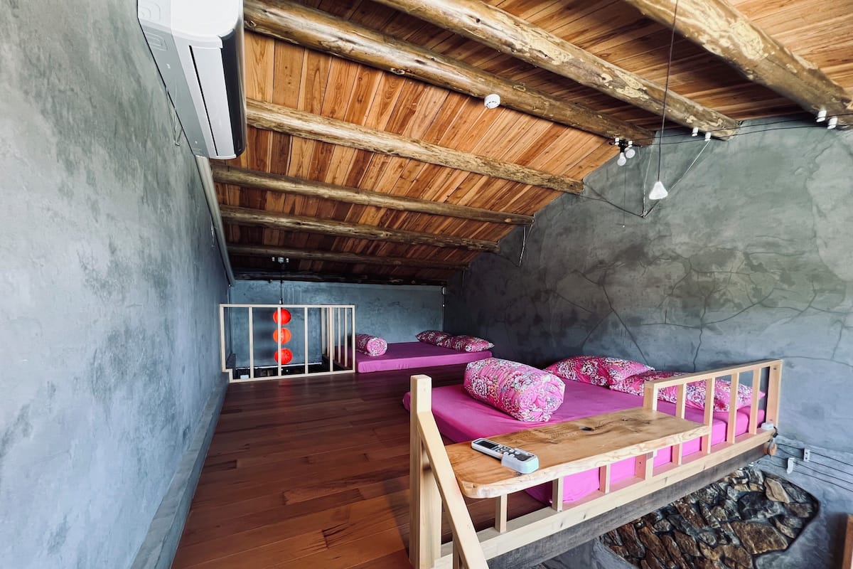 A cozy room with a wooden ceiling, a stone wall, and a bed with pink bedding.